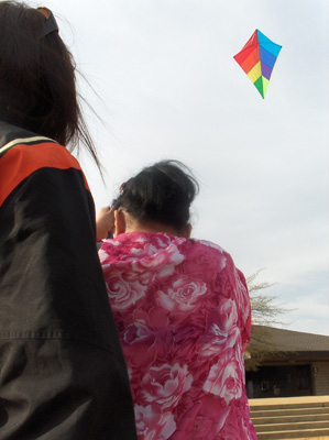 3 photos show Nanta with her arms raised, holding the string of a colorful kite flying above her.